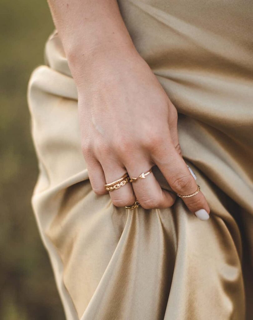 Hand wearing slim gold rings against cream satin